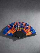 A folding hand fan with a vibrant graphic design featuring blue, orange, and red tones, with the text 'PYRAMID amnesia' and 'ibiza' printed on it. The fan is displayed open against a textured gray background.